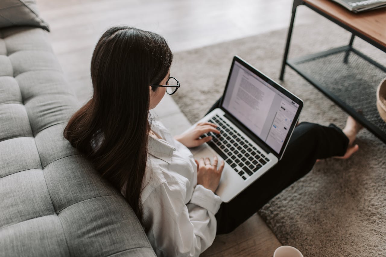 home-hero Woman working remotely with a laptop on the floor next to a sofa, enjoying comfortable home office setup.